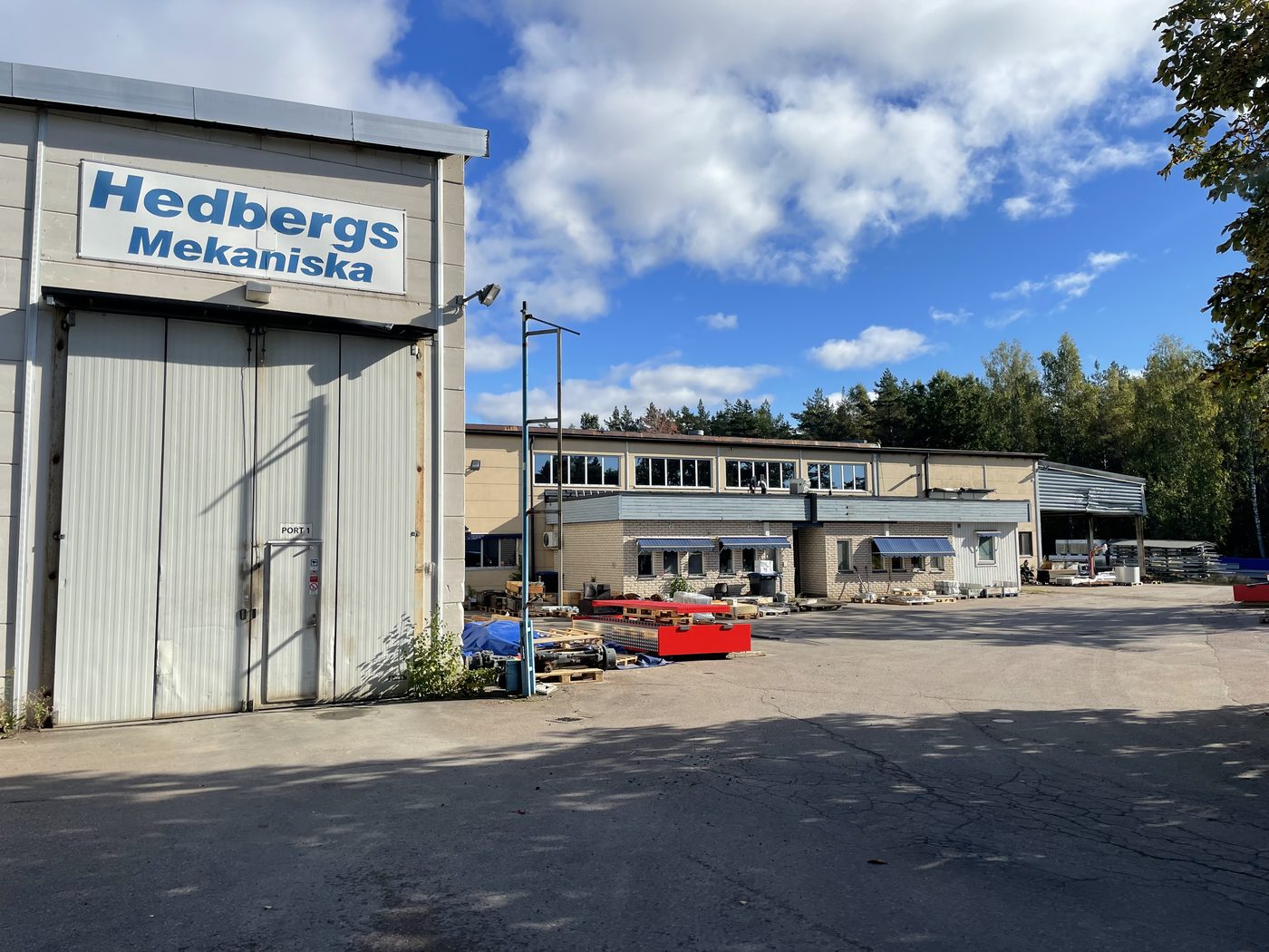 Hedbergs Mekaniskas verkstadsbyggnad med blå skylt, port 1 och asfalterad industritomt